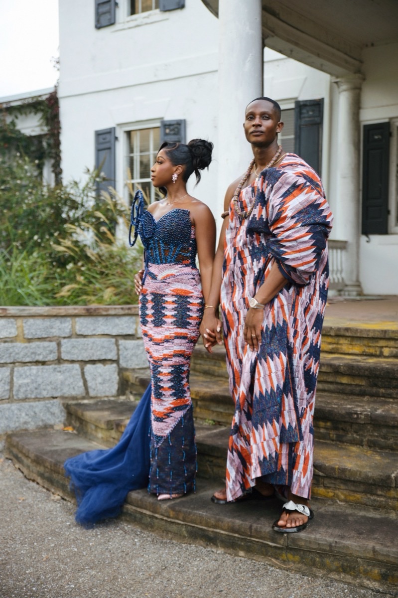 Couple in coordinated kente attire on the steps of a mansion