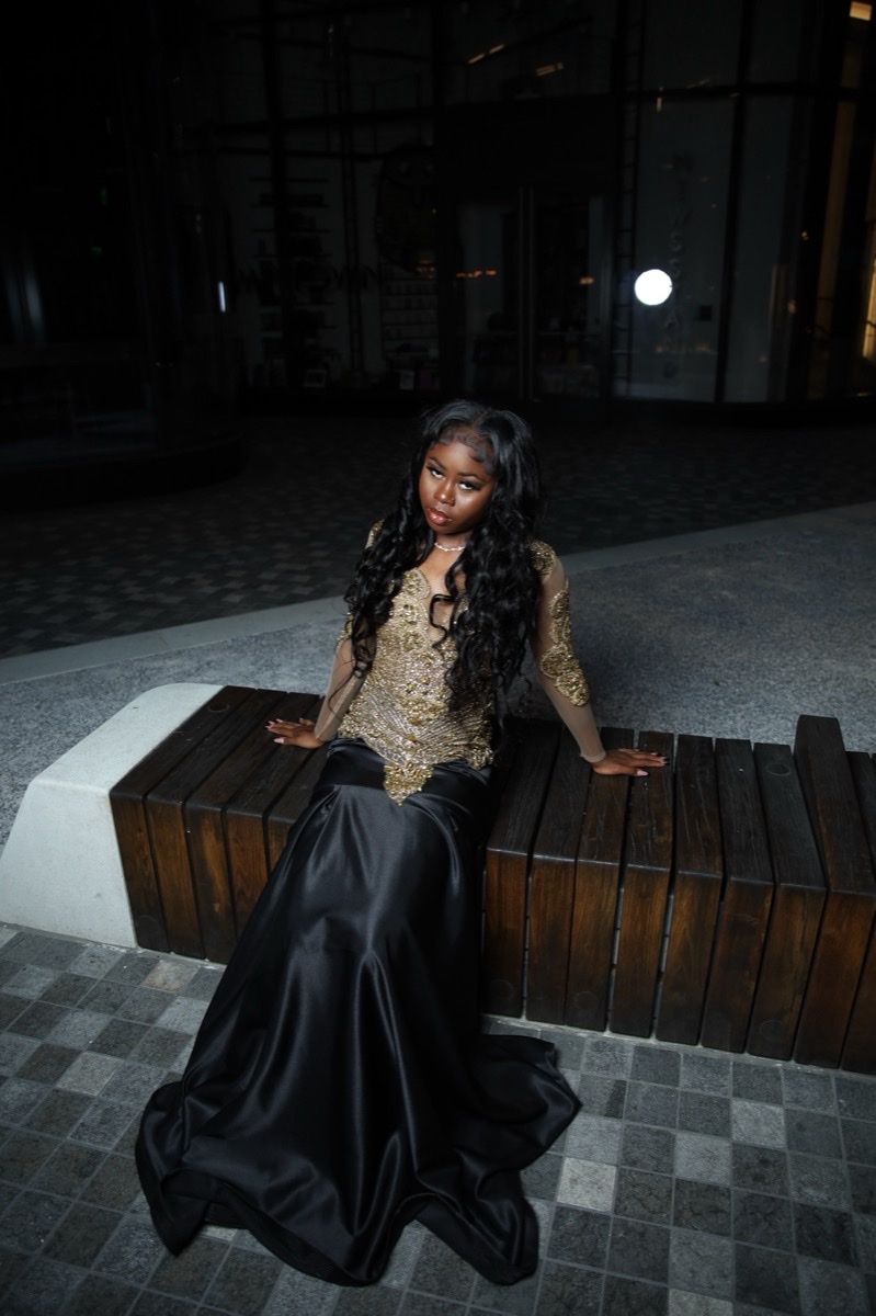 Woman in a black gown seated on a stone bench at night