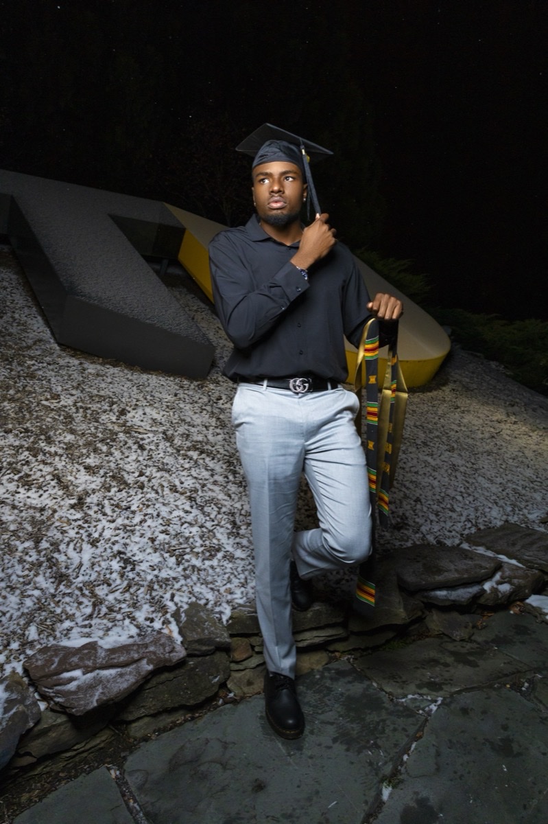 Graduate in cap and gown seated on a stone wall at night