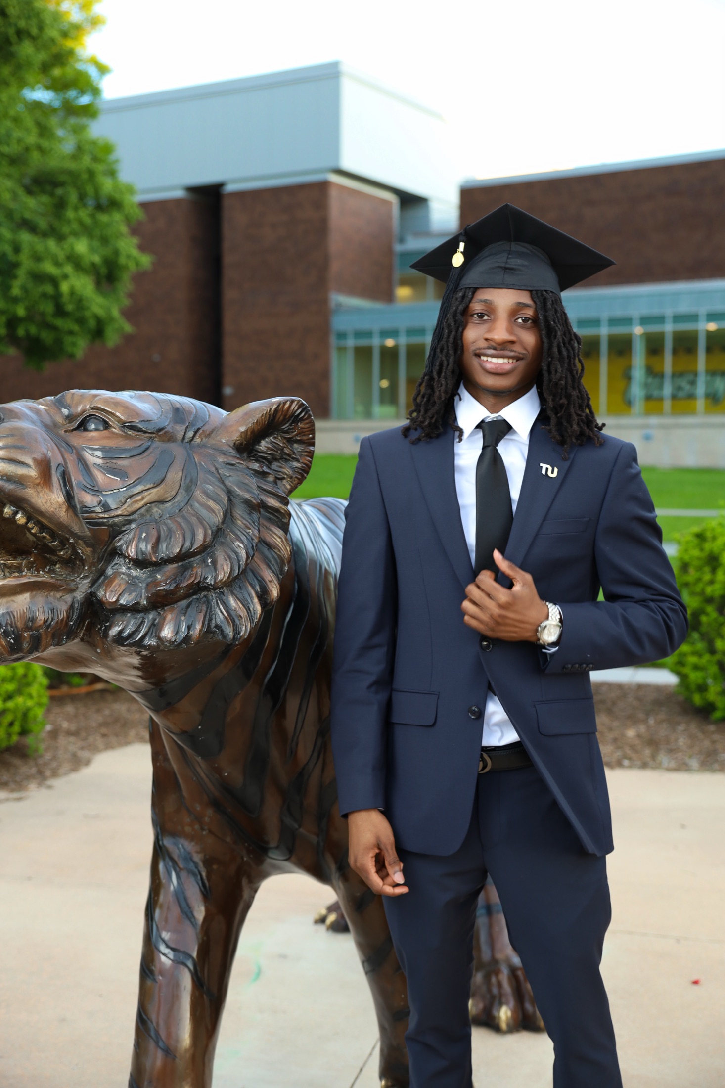 Graduate in a navy suit and cap beside the Towson tiger statue