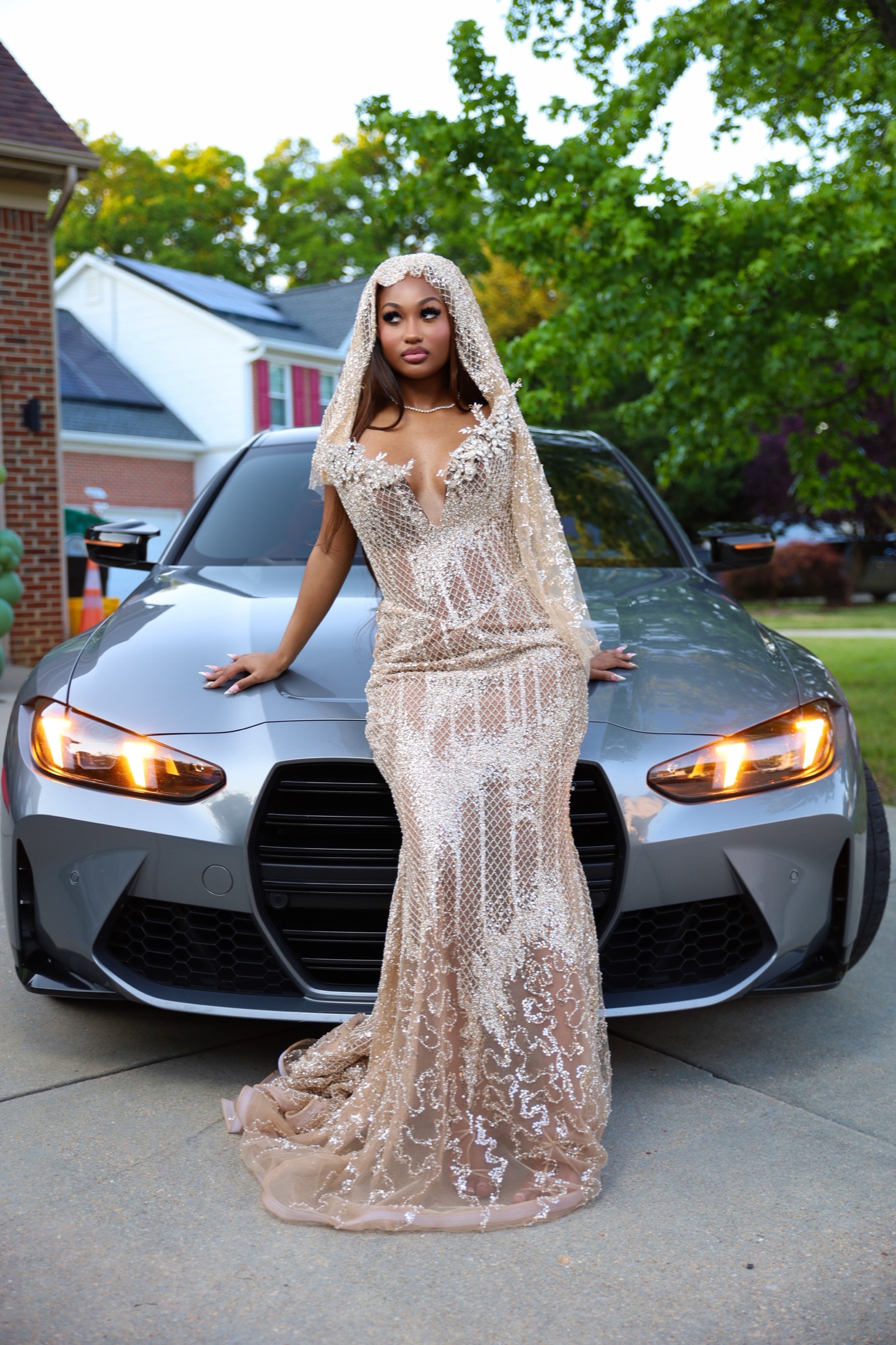 Woman in a gold beaded gown beside a grey sports sedan