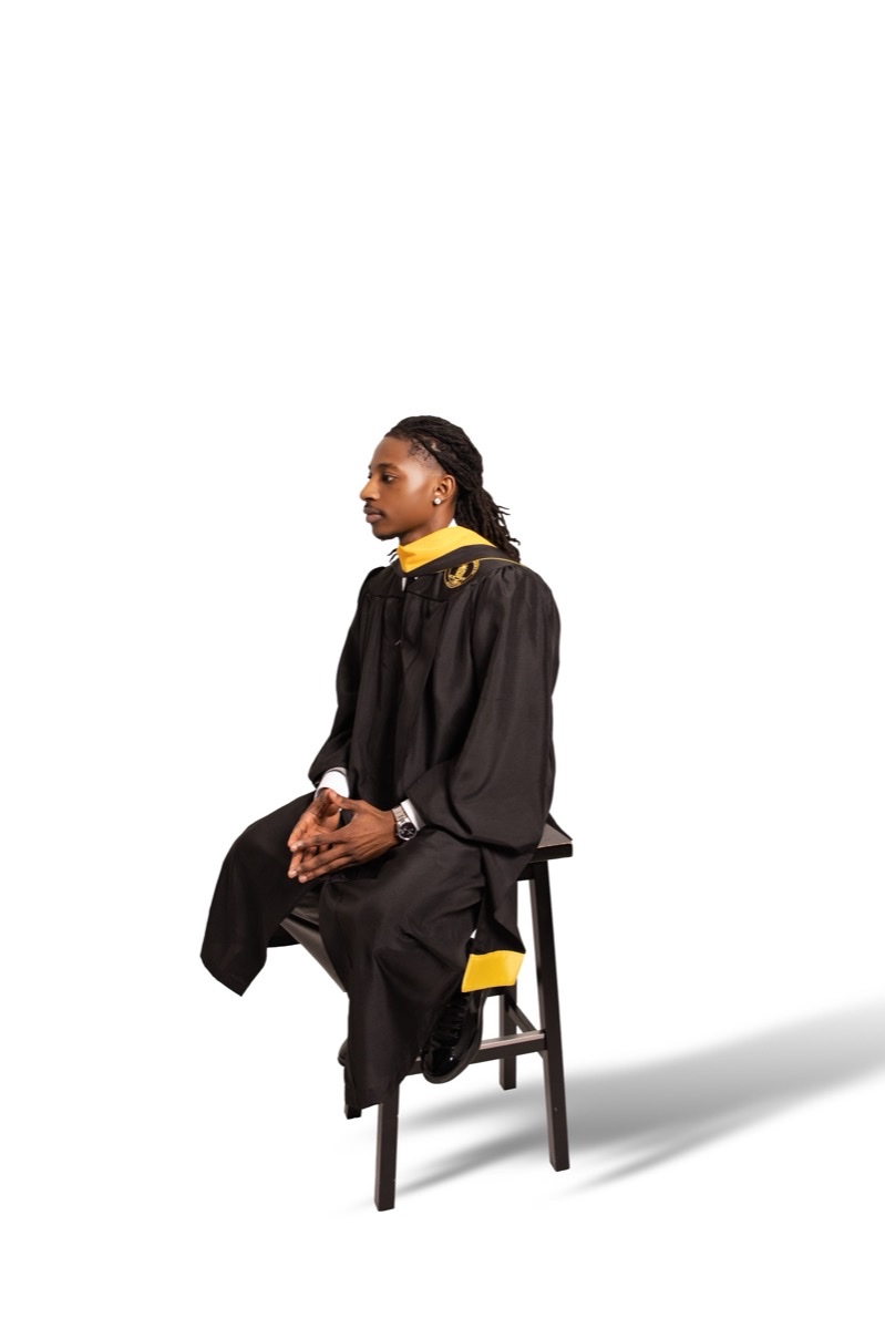 Graduate seated in cap and gown against a white studio backdrop