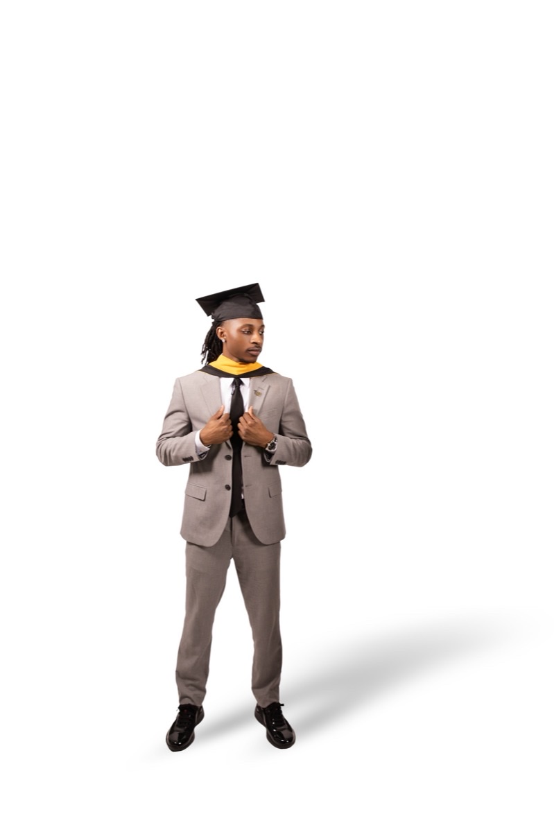 Graduate in a grey suit and gold stole against a white backdrop