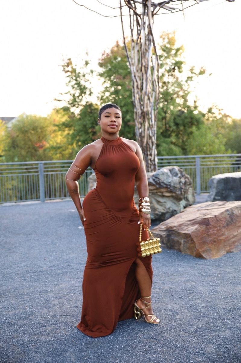 Woman in a rust-colored gown posing against a stone backdrop