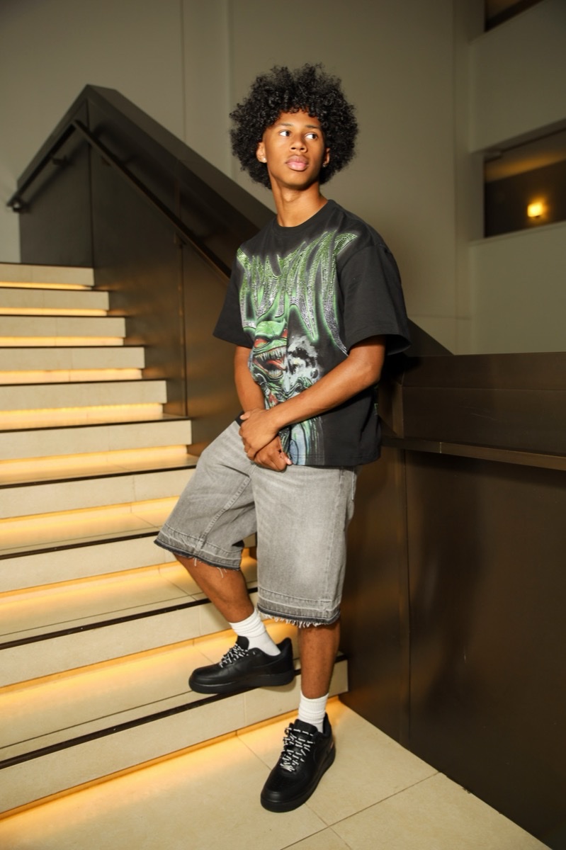 Teen in a graphic tee and denim shorts posing on a lit staircase