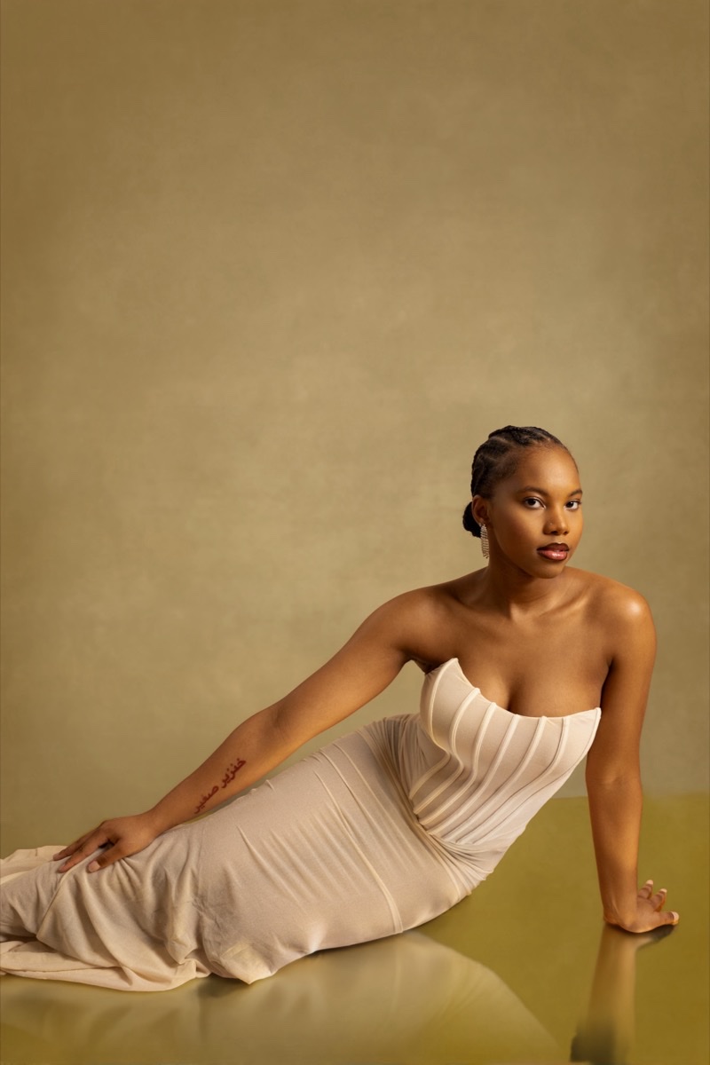Woman in a strapless cream gown reclining on a gold studio backdrop