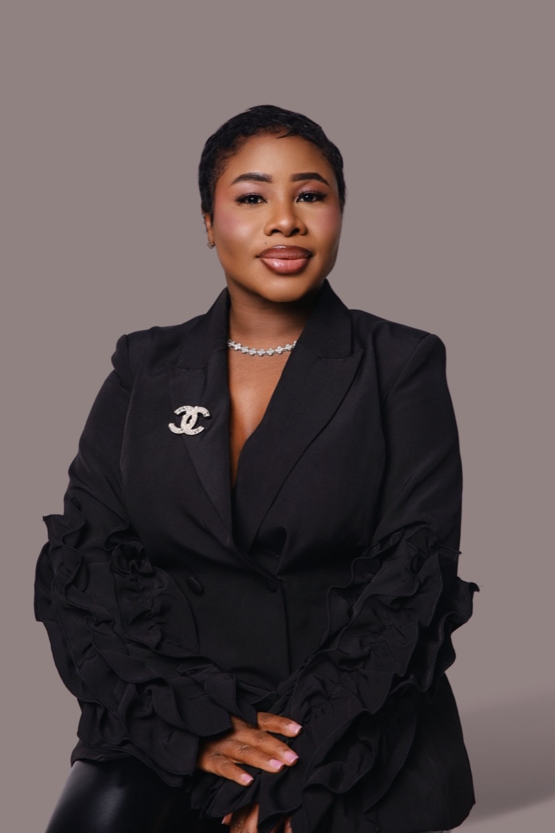 Woman in a black blazer with a brooch, studio headshot
