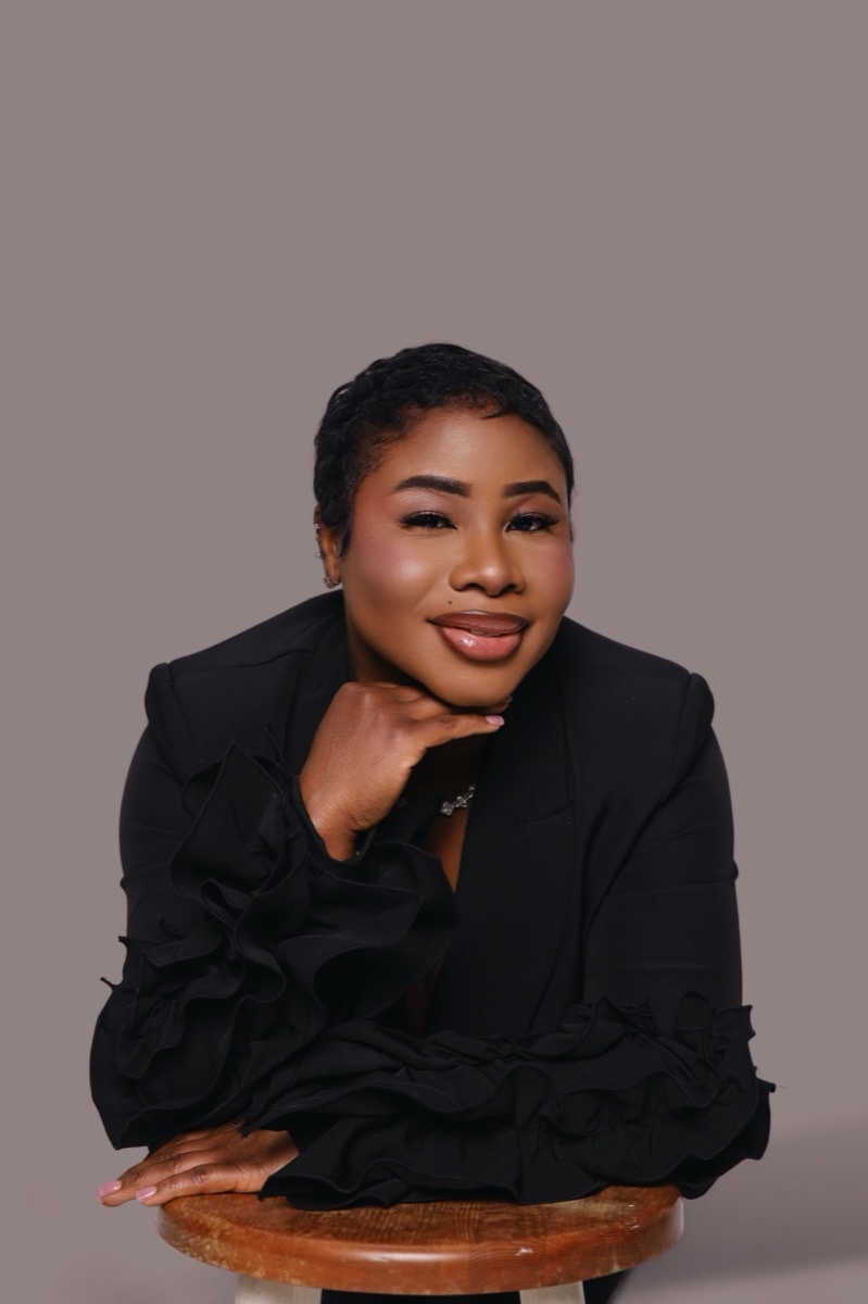 Woman in a black ruffled blazer seated on a stool, studio portrait