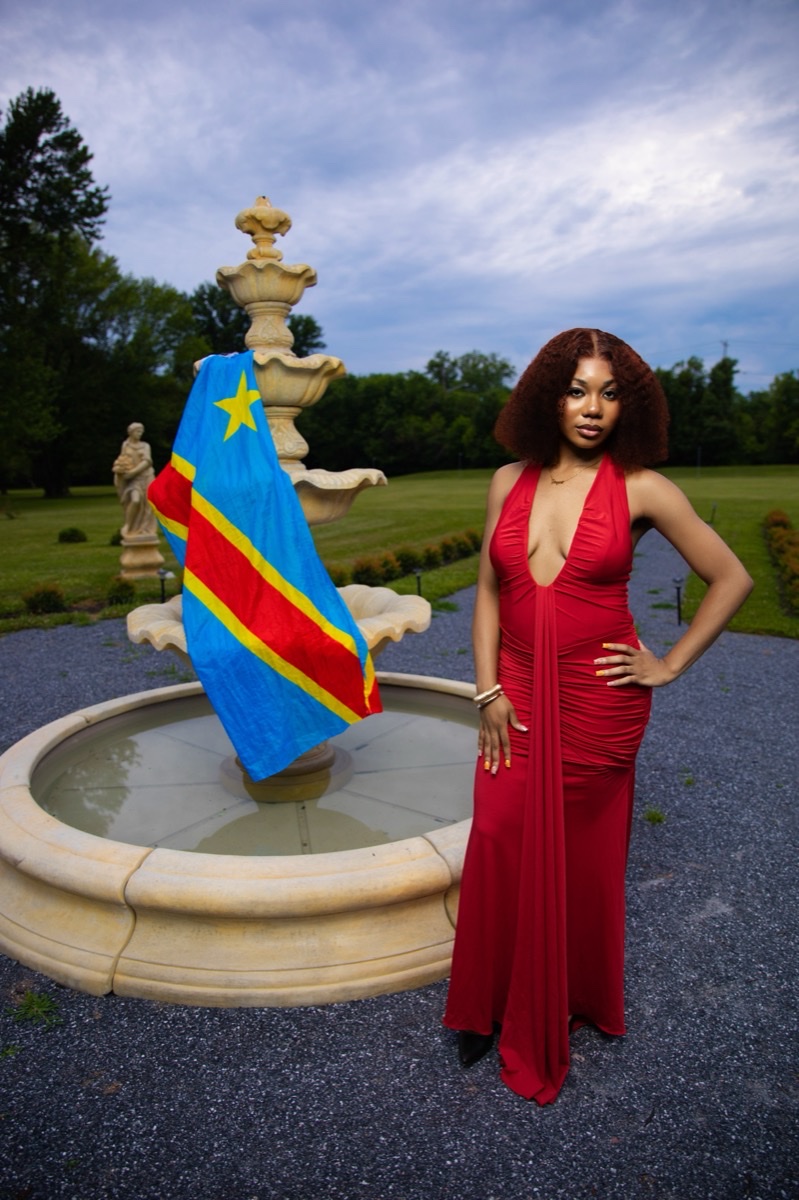 Woman in a red gown posing beside a fountain with a flag