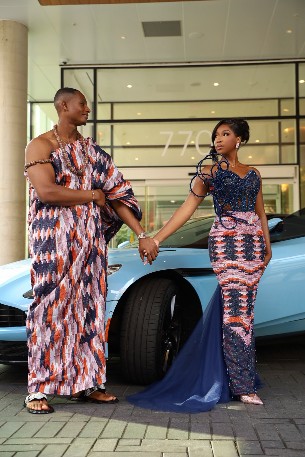 Couple in traditional attire beside a light-blue sports car